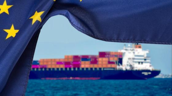 A large trade ship rests on the ocean with the EU flag flying in the foreground