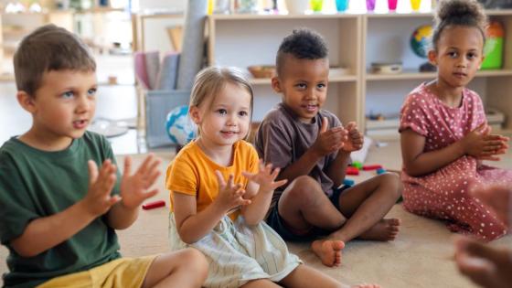 Children sit in a pre-school classroom clapping their hands as part of an exercise