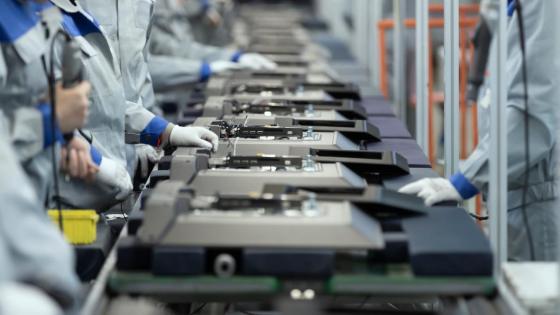 Factory workers inspect electronics on a conveyor belt