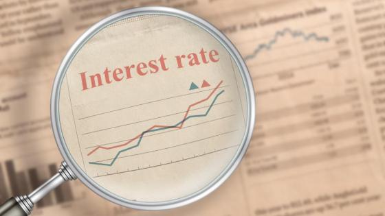 A magnifying glass hovers over the words 'Interest Rate' on a newspaper