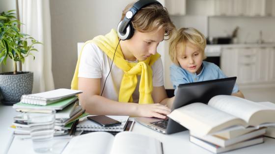 Student studying at home next to younger brother