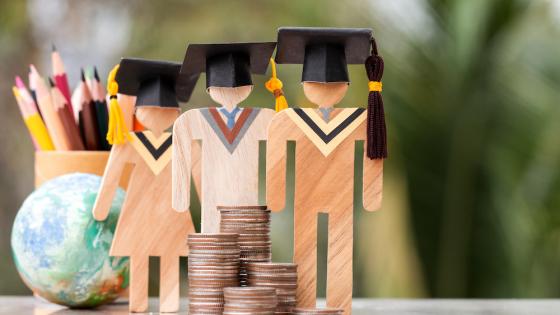 Wooden figures wearing graduate caps and stack of coins
