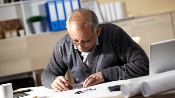 Senior architect working on construction blueprint in office