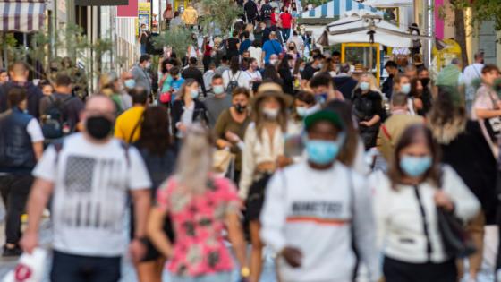 crowd goes up and down a busy shopping street wearing protective masks