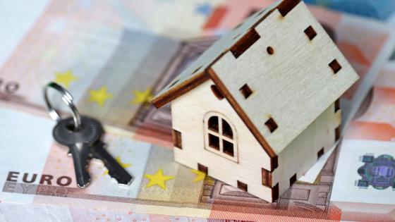 Wooden house model and keys on background of euro banknotes. 