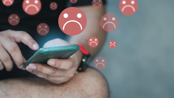 Man using mobile phone surrounded by sad face emojis