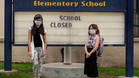 Two schoolgirls in masks in front of a school closed sign