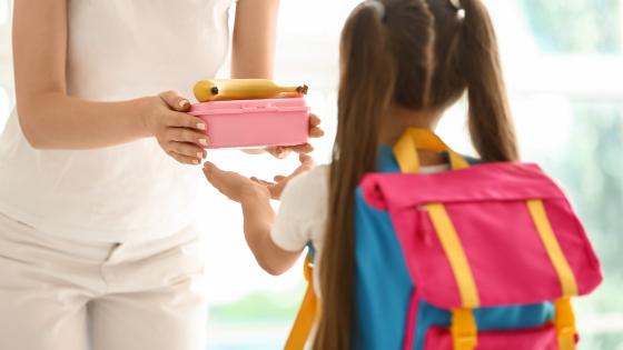 Mother giving lunch box to her little daughter before school