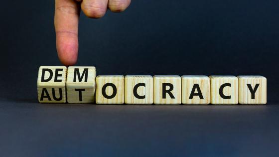Hand turns wooden cubes and changes the word autocracy to democracy. 