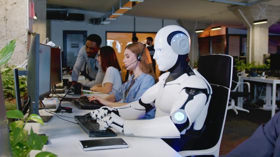 Robot sitting at computer in office