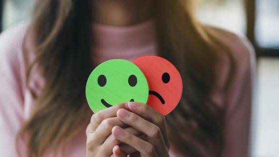A woman holds a green smiley face and a red sad face