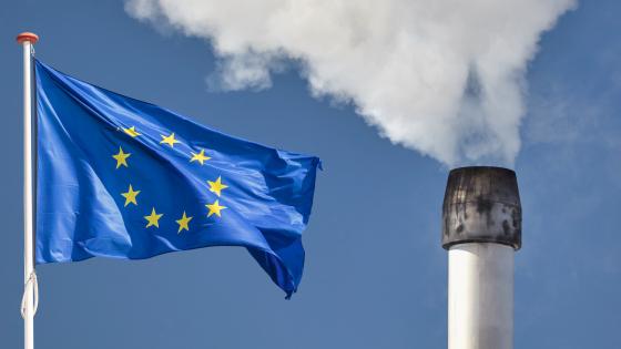EU flag next to factory chimney emitting smoke