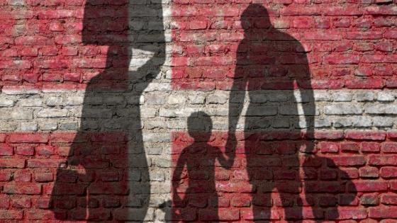 Silhouettes of refugees against a brick wall painted the colour of the Danish Flag