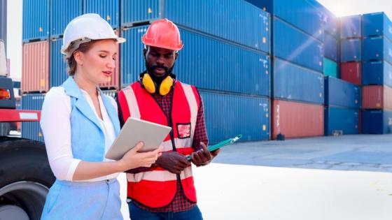 A woman explains something to a male worker with containers in the background