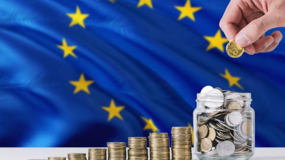 Stacks of euro coins next to jar containing euros in front of EU flag