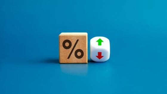 Percentage icon on wooden cube block and up and down arrow symbol on flipping white dice on blue background.