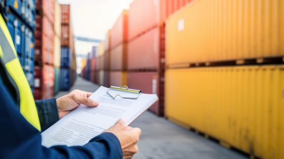 Person holding clipboard in front of shipping containers