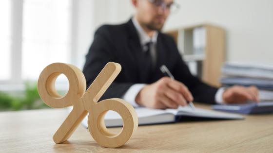 Wooden percentage sign in front of man in suit sitting at a desk