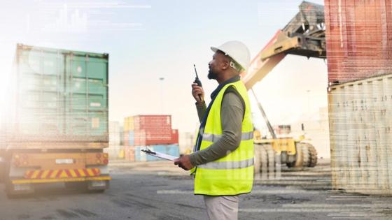 A worker talks on a walkie talkie among trade containers