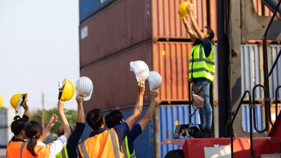 Worker addressing crowd in front of shipping containers